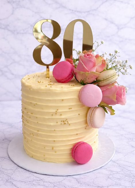 80th birthday cake with gold topper and pink macarons
