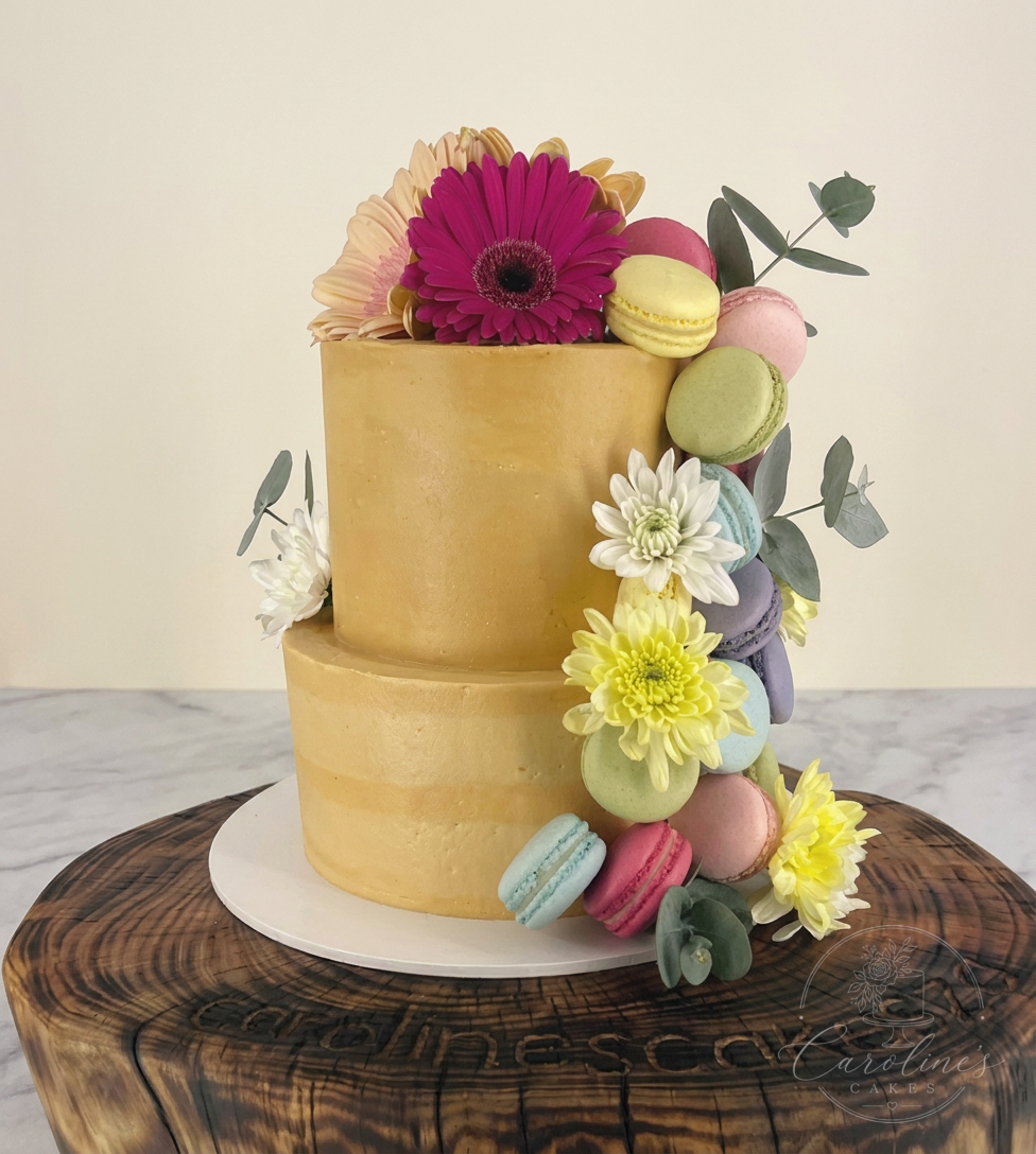 Two-tier gold buttercream cake cascading with macarons and gerberas